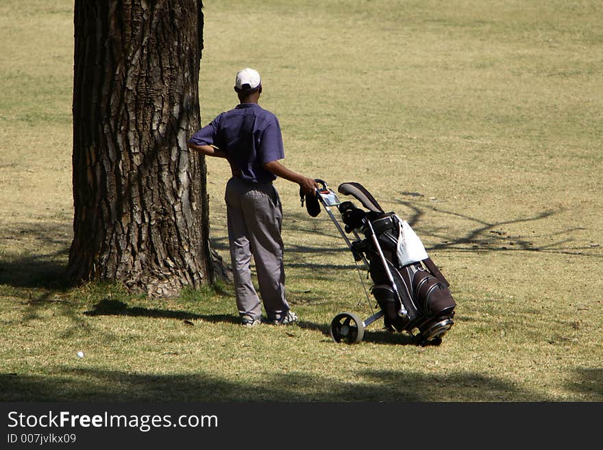 Golfer waiting to play standin next to a tree