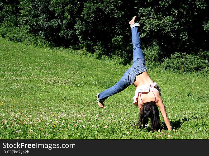 A young woman makes a handstand on grass in front of blue sky