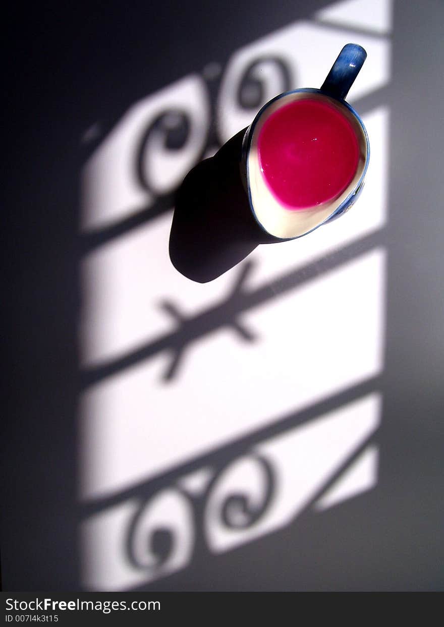 The shadow of the bars and barroque forms of an old window is softly casted over an old porcelain blue and white jar with a pink liquid. The ilumination is from natural light at afternoon. The shadow of the bars and barroque forms of an old window is softly casted over an old porcelain blue and white jar with a pink liquid. The ilumination is from natural light at afternoon.