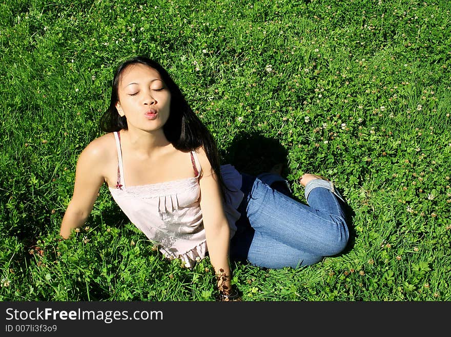 Asian young woman with long black hair sitting on grass is kissing. Asian young woman with long black hair sitting on grass is kissing