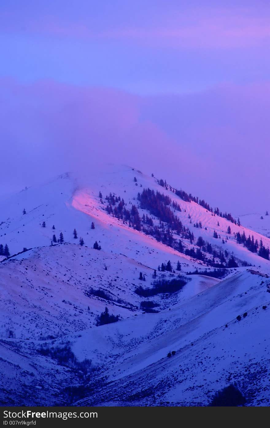 Snow covered mountains peaks with soft pink sunset, sunrise sunlight light on it with clouds. Snow covered mountains peaks with soft pink sunset, sunrise sunlight light on it with clouds