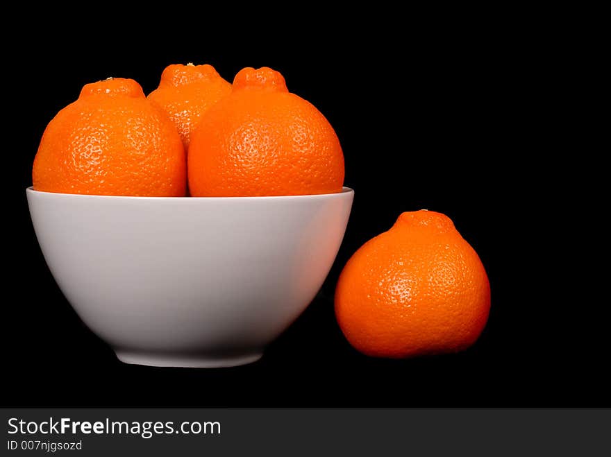 Three minneola oranges in white bowl with one orange at side