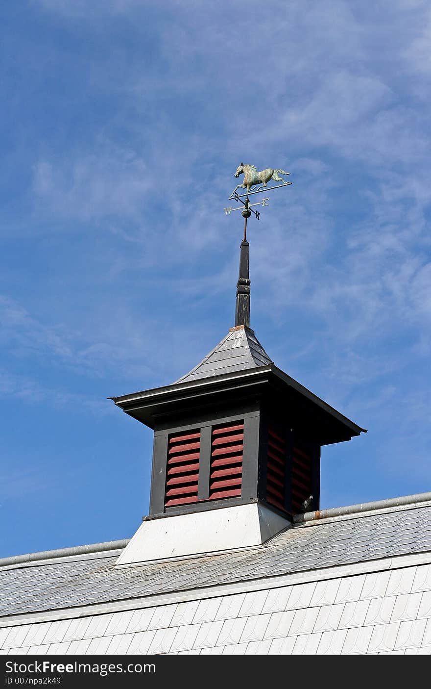 Copper horse weathervane on a barn's cupola that has green patina.