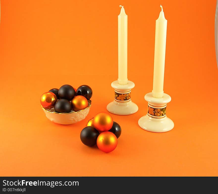 Bowl filled with orange and black balls, add candlesticks and candles all on an orange background. Bowl filled with orange and black balls, add candlesticks and candles all on an orange background.