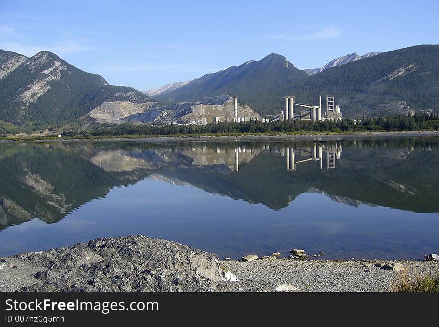 The landscape with factory on the bank, reflection of the mountains on the lake