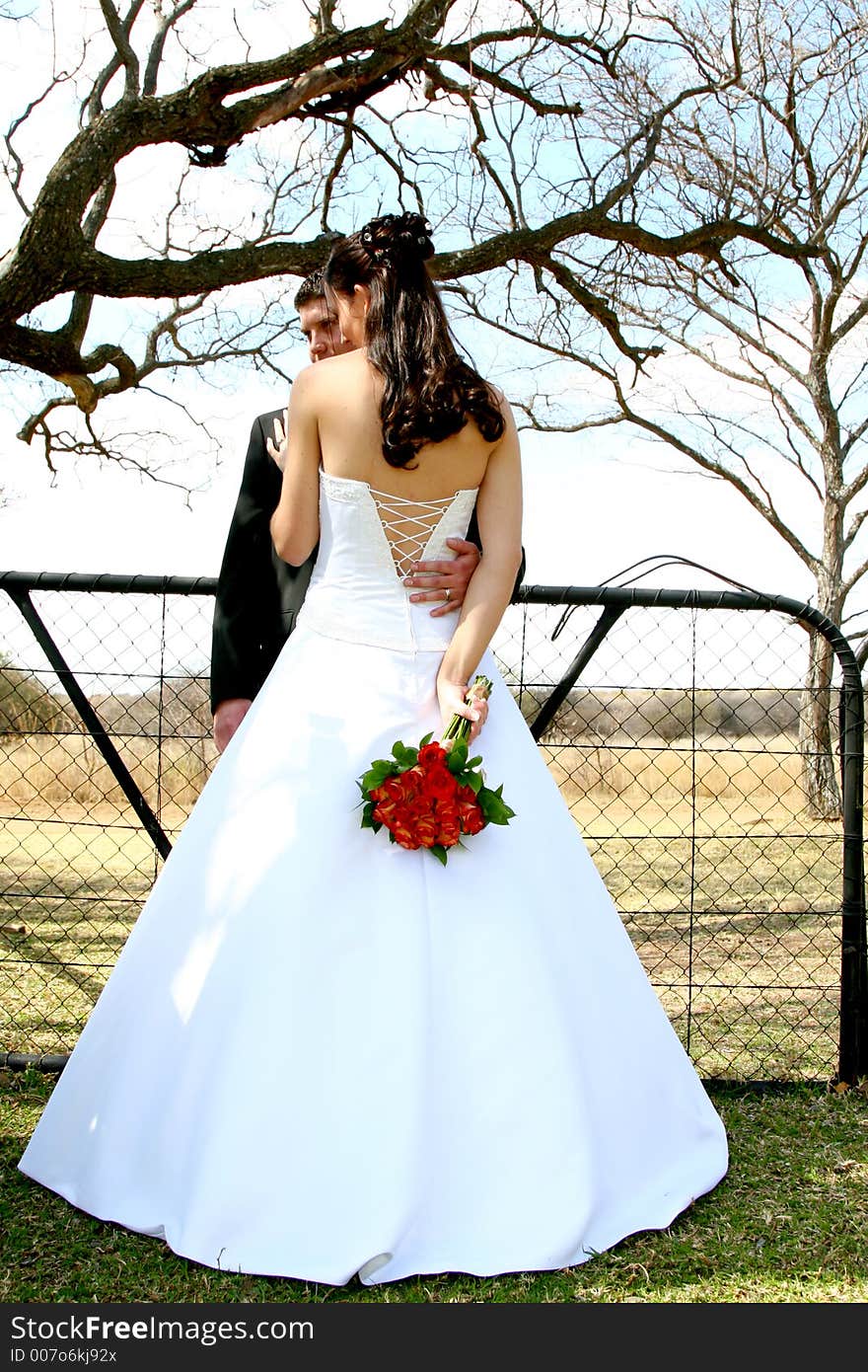 Bride and groom standing by a fence. Bride and groom standing by a fence