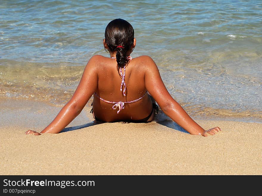 A teenager girl is sitting on the beach with feet in the water. A teenager girl is sitting on the beach with feet in the water