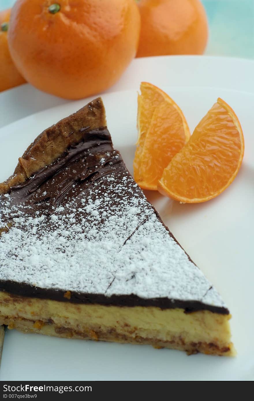 An angle view of a slice of chocolate mocha and orange cheesecake. Table setting with mandarin oranges for styling. Hue adjusted. An angle view of a slice of chocolate mocha and orange cheesecake. Table setting with mandarin oranges for styling. Hue adjusted.