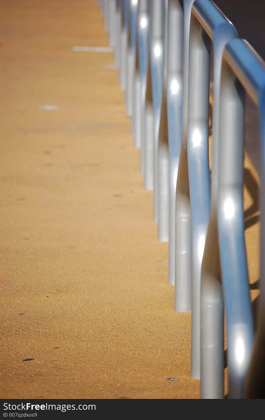 Tram stop railing with metal guards reflecting the blue sky and orange gravel