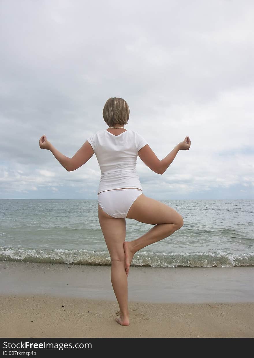 Woman in white standing in yoga tree pose at the beach