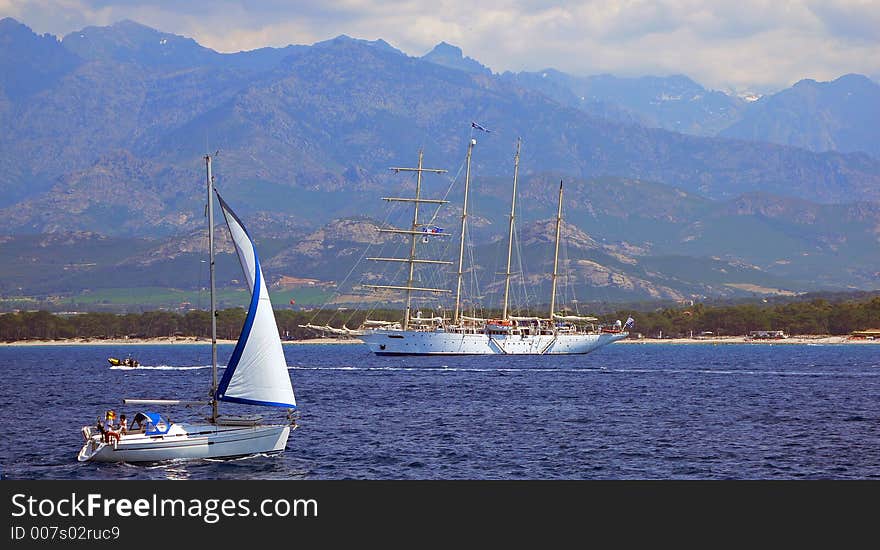 A sailboat passing in front of a clipper tall ship in the bay of Calvi. A sailboat passing in front of a clipper tall ship in the bay of Calvi