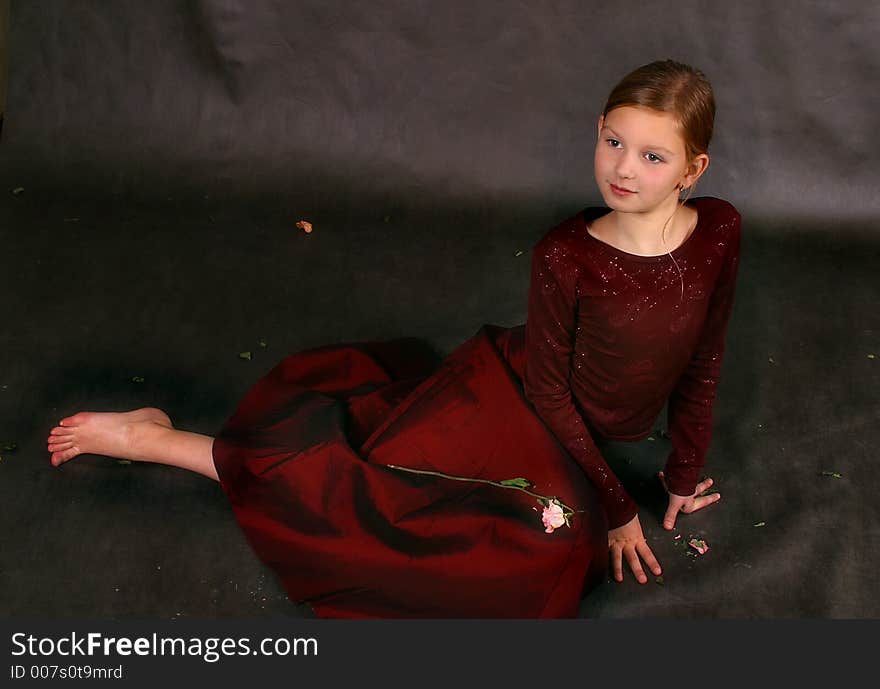 The girl in a red dress and barefoot sits on a floor in studio. The girl in a red dress and barefoot sits on a floor in studio