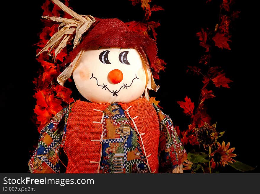 A Halloween Scarecrow or autumn scarecrow among autumn leaves and sunflowers.