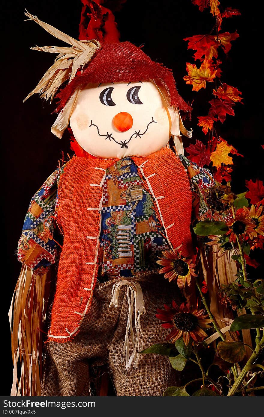 A Halloween Scarecrow among autumn leaves and sunflowers.