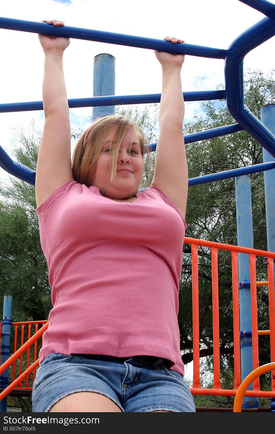 Teenage girl hanging from the monkey bars at a park. Teenage girl hanging from the monkey bars at a park.