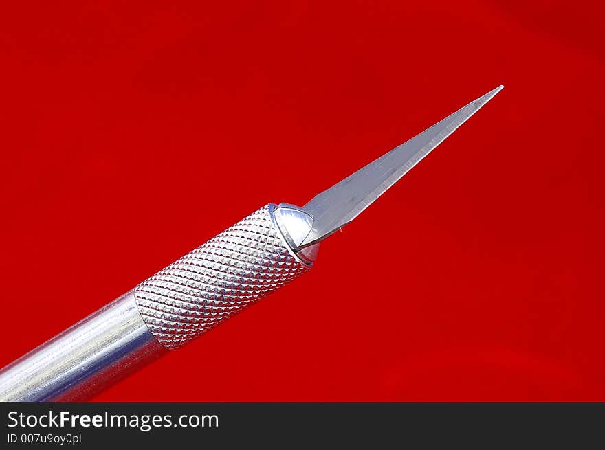 Closeup of a hobby knife blade against a bright red background. Closeup of a hobby knife blade against a bright red background