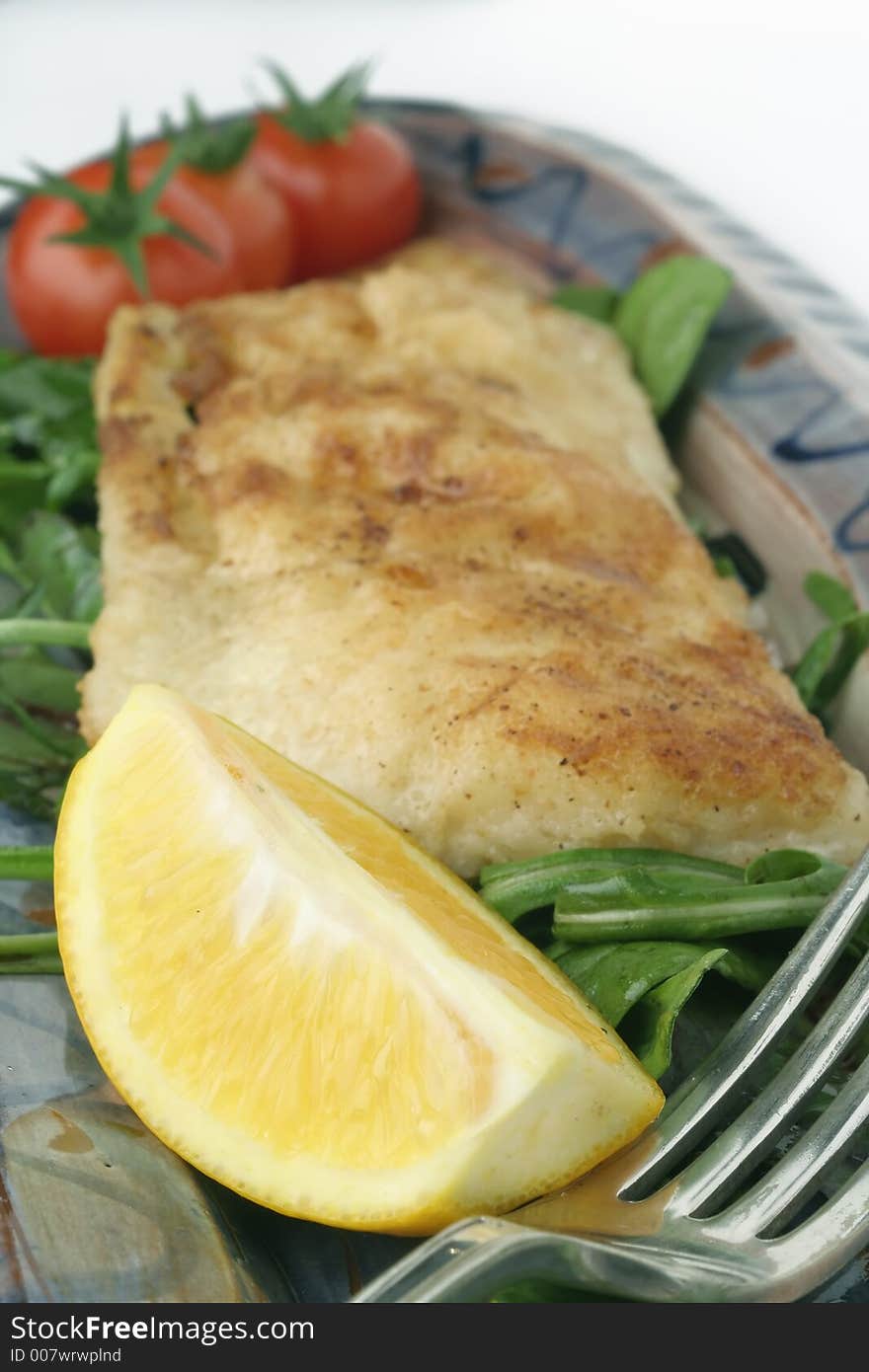 A close shot of a fish snack consisting of grilled and battered bream, rocket and cherry tomato salad with a larger slice of lemon. Shallow depth of field. A close shot of a fish snack consisting of grilled and battered bream, rocket and cherry tomato salad with a larger slice of lemon. Shallow depth of field.