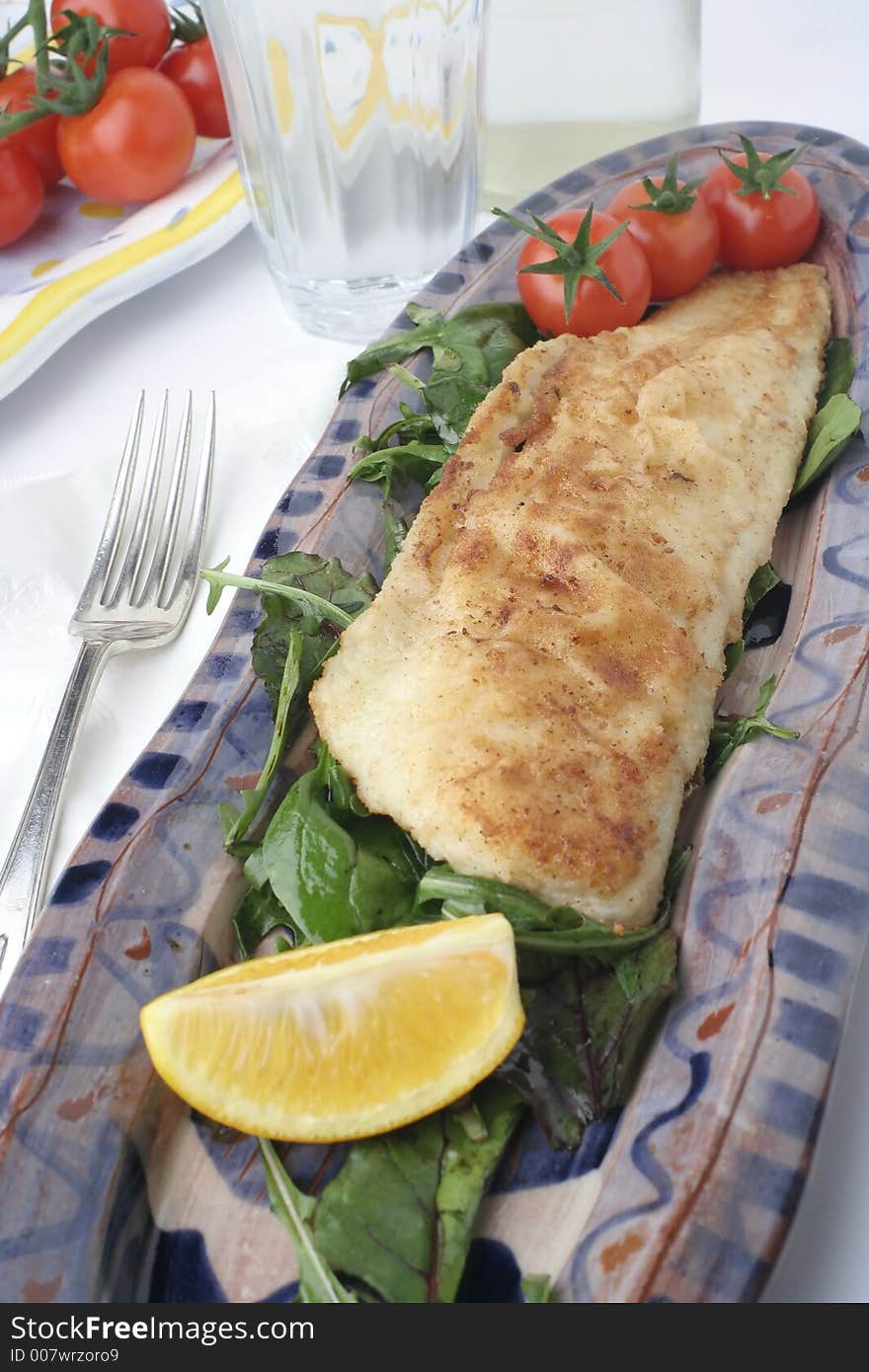 Glazed earthenware platters with grilled and battered bream with rocket salad. Cherry tomato side plate. Glass of water and water bottle. Glazed earthenware platters with grilled and battered bream with rocket salad. Cherry tomato side plate. Glass of water and water bottle.