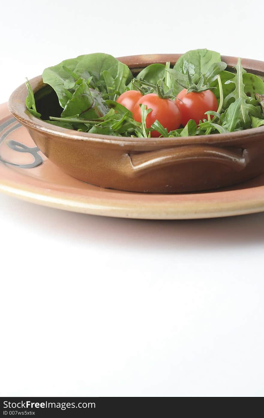 A mixed green salad and cherry tomatoes in a stoneware casserole sitting on a stoneware platter. A mixed green salad and cherry tomatoes in a stoneware casserole sitting on a stoneware platter.