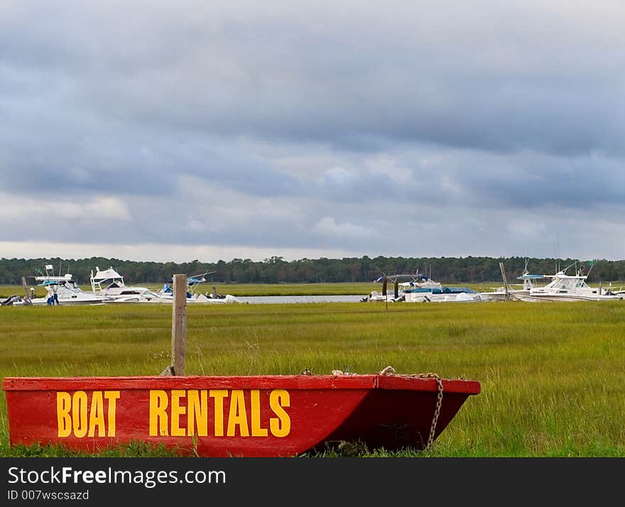 Rental Boats on small boat sitting by the road with large boats (in the water) in the background. Rental Boats on small boat sitting by the road with large boats (in the water) in the background