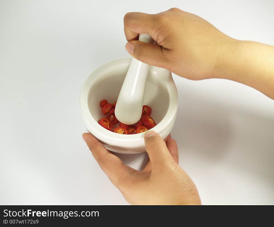 Grinding red chillies in a white mortar and pestle. Grinding red chillies in a white mortar and pestle