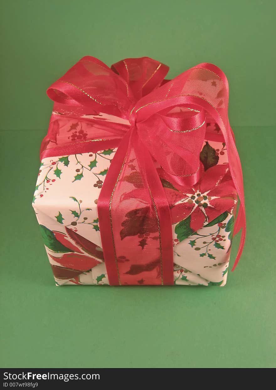 Christmas present wrapped in poinsettia pattern paper and a red bow; green background. Christmas present wrapped in poinsettia pattern paper and a red bow; green background.