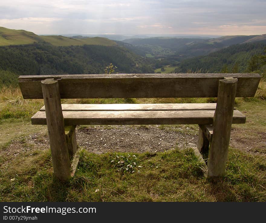 Wooden bench on mountain in Wales with view of hills and ocean in distance