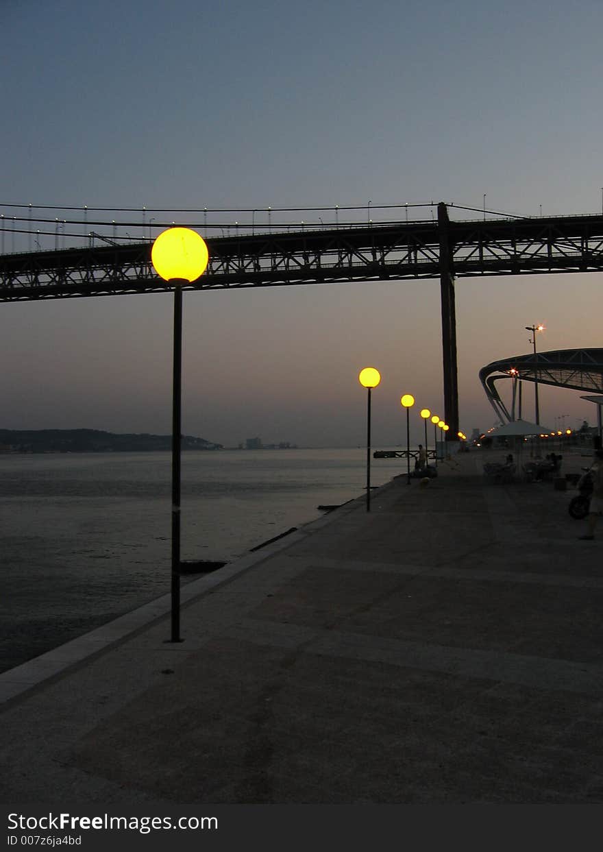 The Tejo river, the bridge and the street lamps at dusk in Lisbon. The Tejo river, the bridge and the street lamps at dusk in Lisbon.