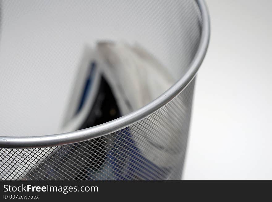 A wire waste paper basket with an out of focus discarded newspaper. A wire waste paper basket with an out of focus discarded newspaper