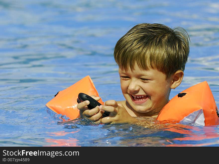 Boy child makes a call with a cell-phone in a swimming-pool. Boy child makes a call with a cell-phone in a swimming-pool