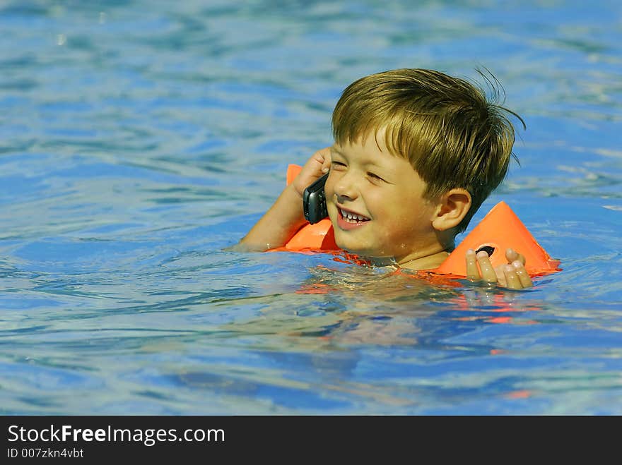 Boy child makes a call with a cell-phone in a swimming-pool. Boy child makes a call with a cell-phone in a swimming-pool