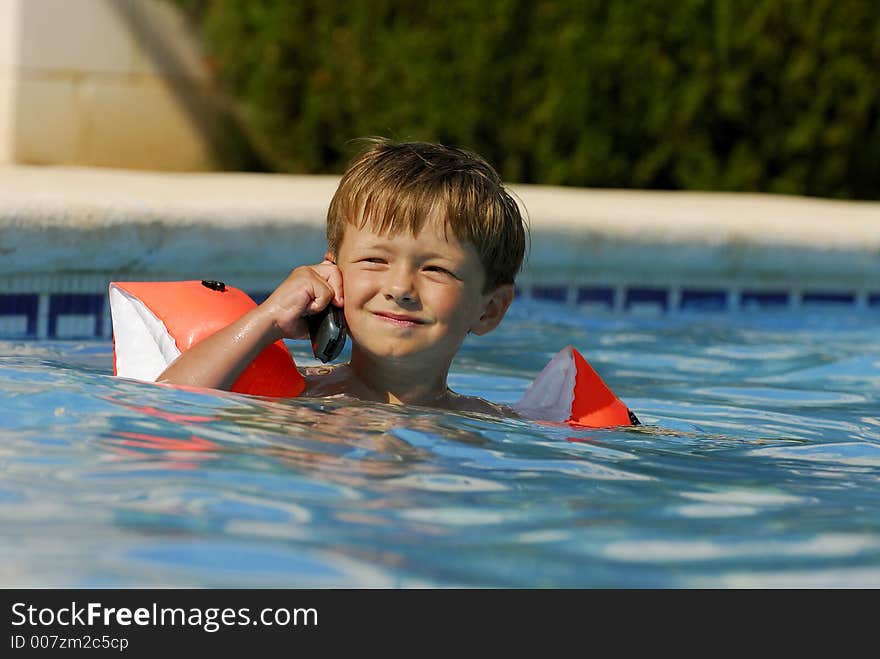 Boy child makes a call with a cell-phone in a swimming-pool. Boy child makes a call with a cell-phone in a swimming-pool