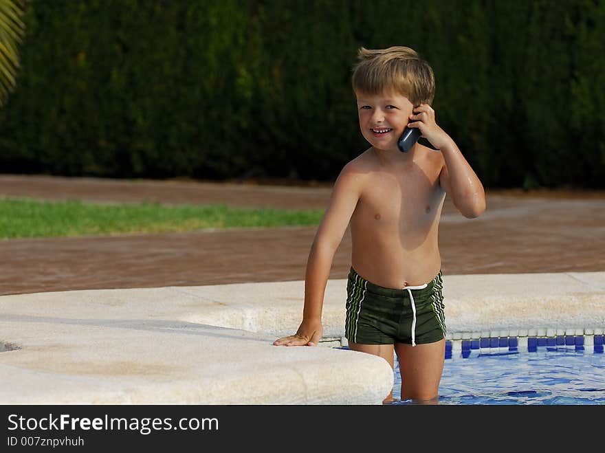 Boy child makes a call with a cell-phone standing in a swimming-pool. Boy child makes a call with a cell-phone standing in a swimming-pool