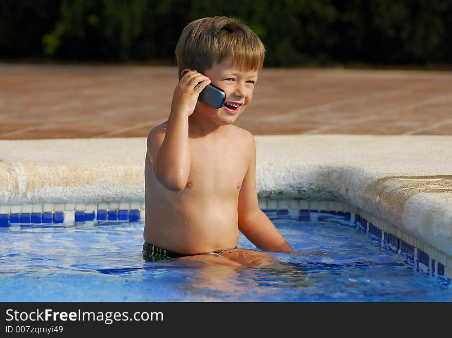 Boy child makes a call with a cell-phone sitting in a swimming-pool. Boy child makes a call with a cell-phone sitting in a swimming-pool