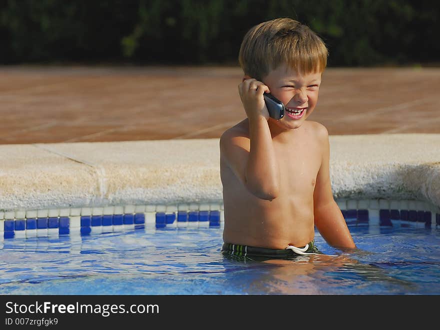 Boy child makes a call with a cell-phone sitting and laughing in a swimming-pool. Boy child makes a call with a cell-phone sitting and laughing in a swimming-pool