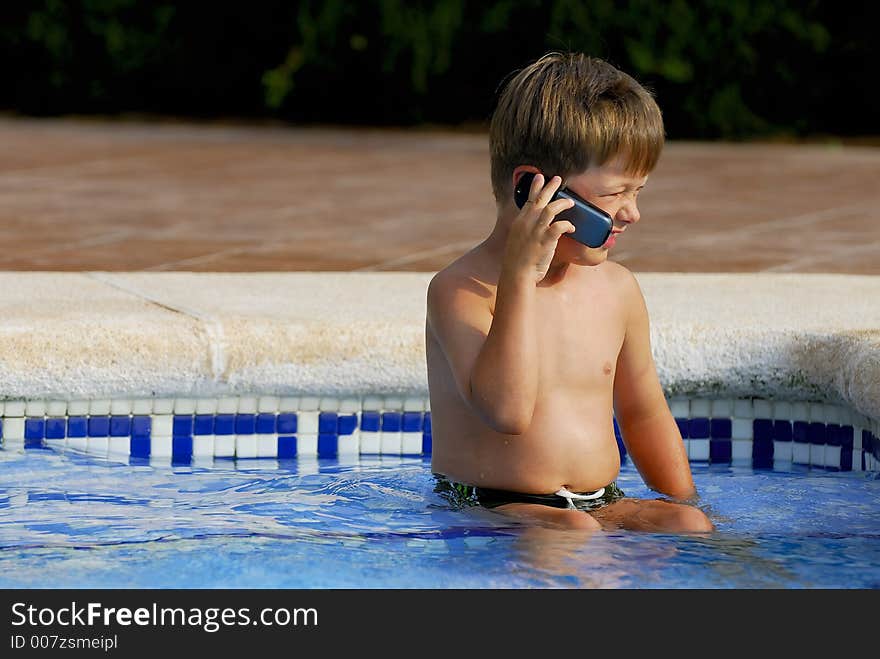 Boy child makes a call with a cell-phone sitting in a swimming-pool. Boy child makes a call with a cell-phone sitting in a swimming-pool