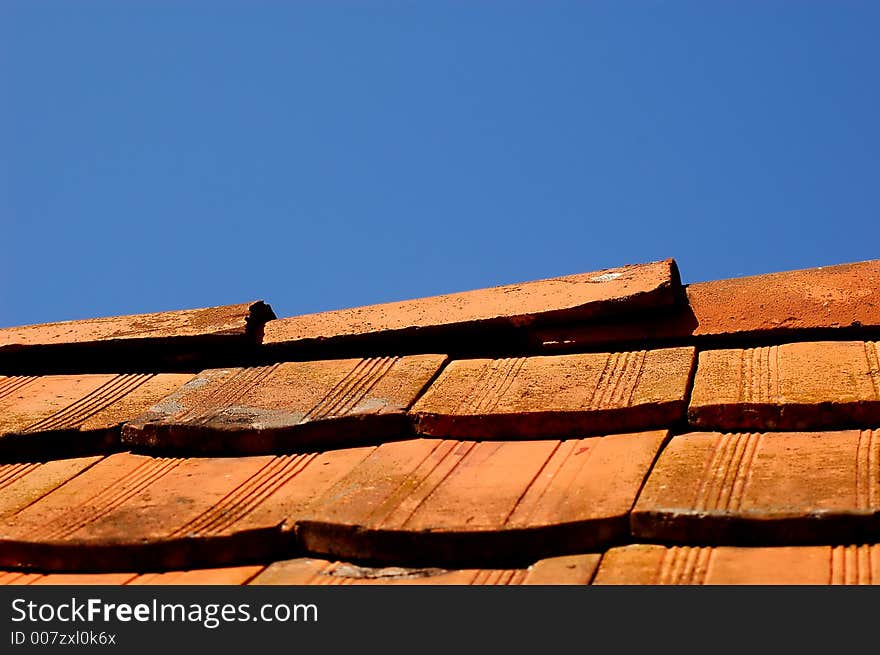 Orange/red roof of old country house with blue sky as background. Orange/red roof of old country house with blue sky as background