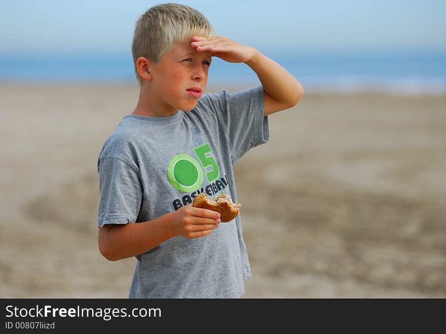 Young boy is watching the scenery at the beach and is eating a hamburger. Young boy is watching the scenery at the beach and is eating a hamburger