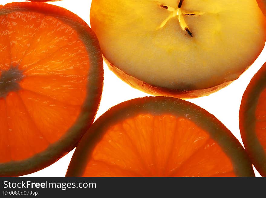 Slices of orange and apple on white background, lit from underneath. Slices of orange and apple on white background, lit from underneath