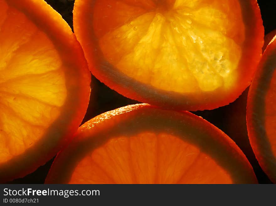 Slices of orange on black background, lit from underneath. Slices of orange on black background, lit from underneath