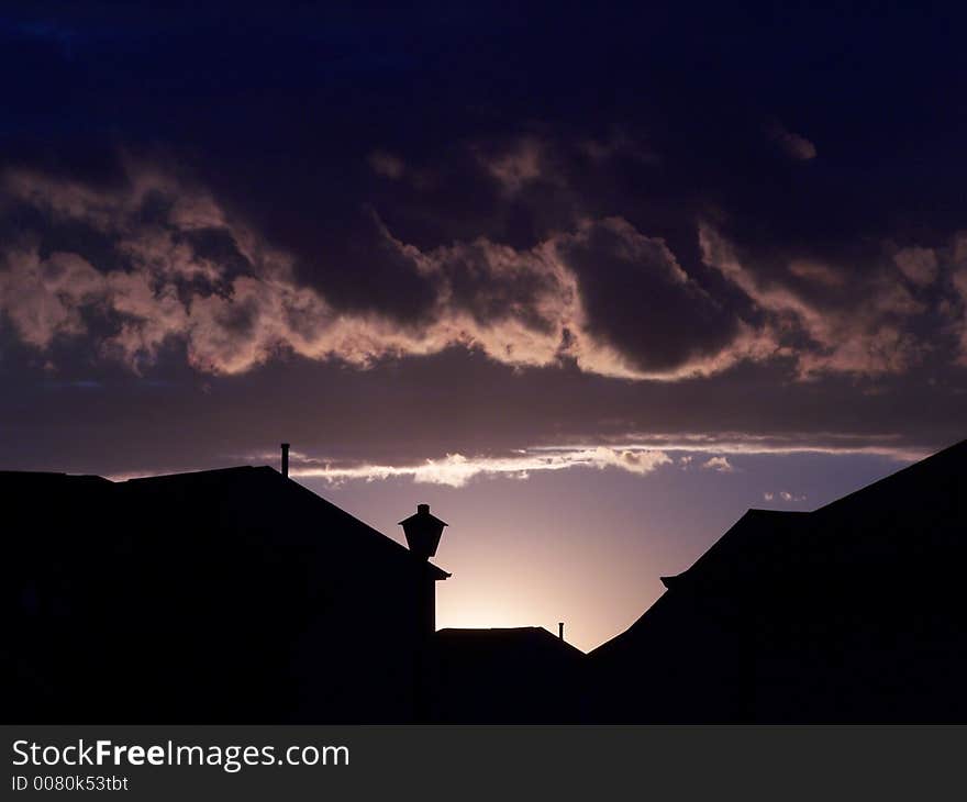 Desaturated photo of setting sun that outlines clouds and residential houses. Desaturated photo of setting sun that outlines clouds and residential houses.