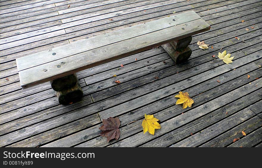 Wooden bench on the deck in the autumnal park with few yellow maple leafs. Wooden bench on the deck in the autumnal park with few yellow maple leafs