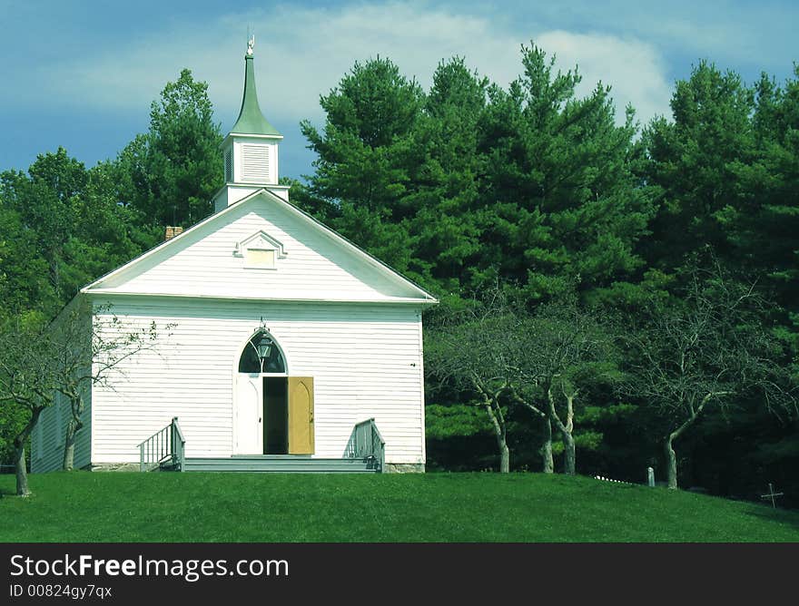 A small country chapel sits on a sunny hill near a forest.