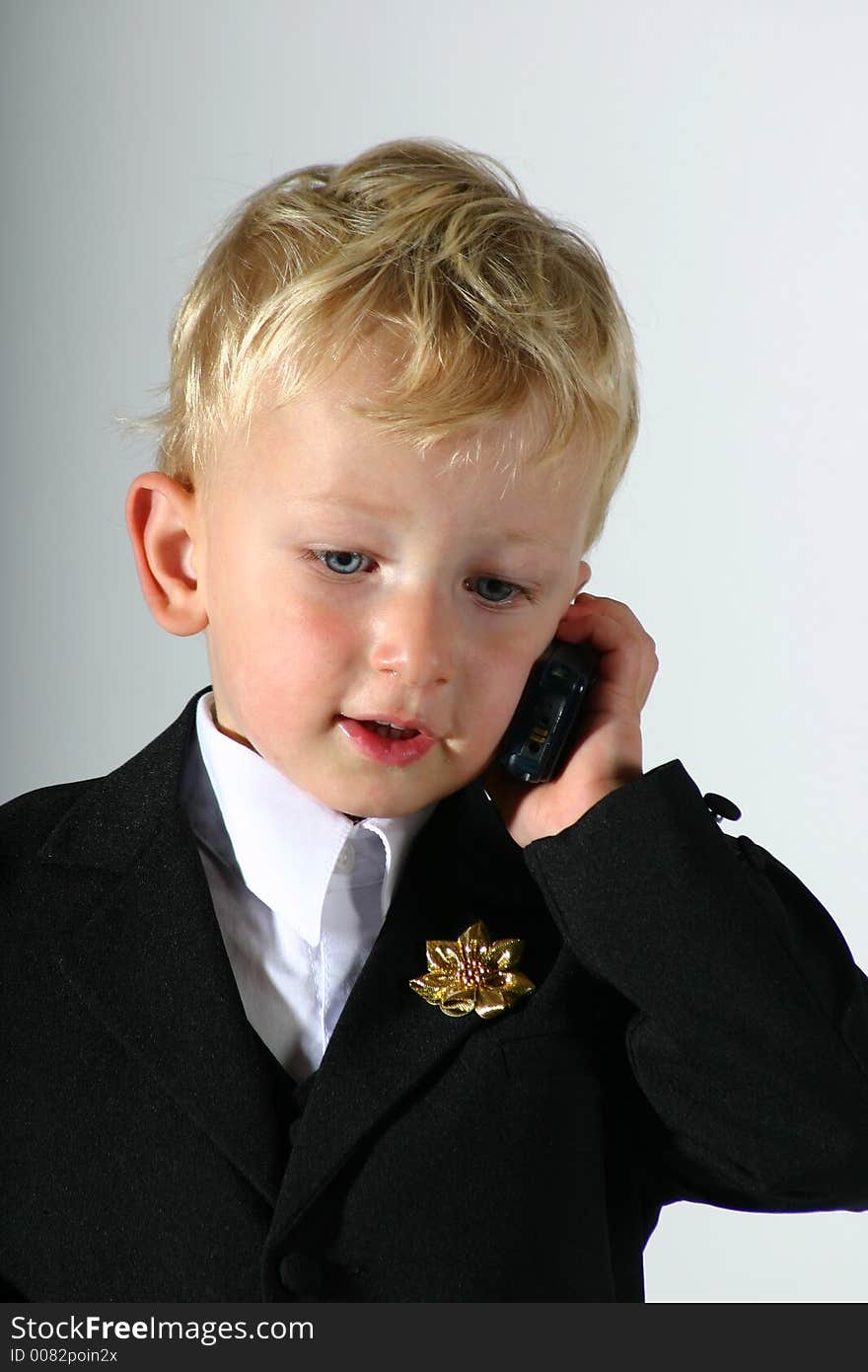 Toddler boy dressed up in black suit and white shirt talking on a mobile phone. Toddler boy dressed up in black suit and white shirt talking on a mobile phone