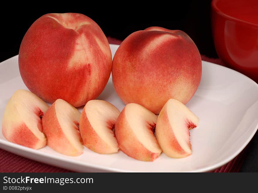 Whole and sliced white peaches on a white plate