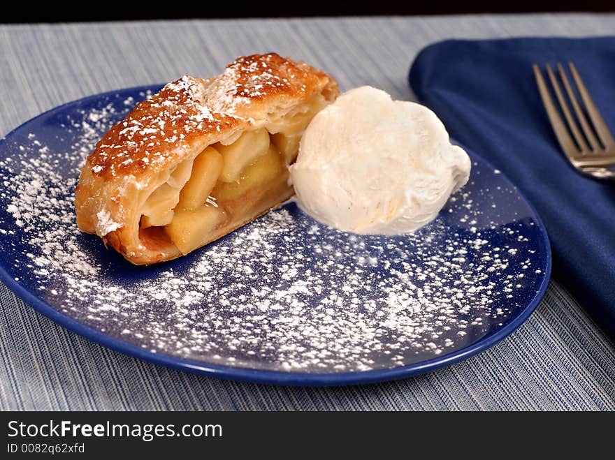 Apple strudel with vanilla ice cream on a blue plate dusted with powdered sugar