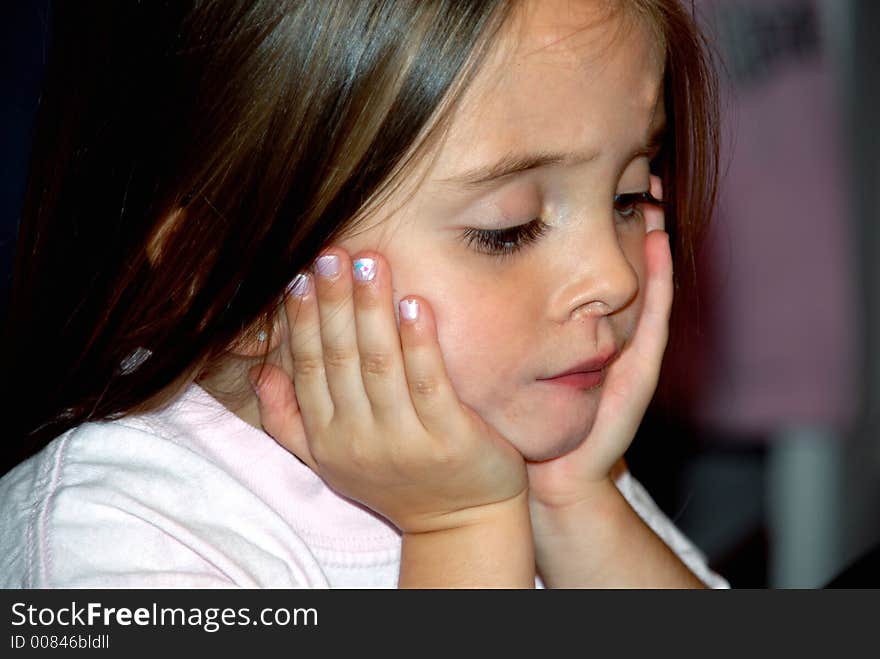 A beautiful young girl looking down with her hands on her face in deep thought.