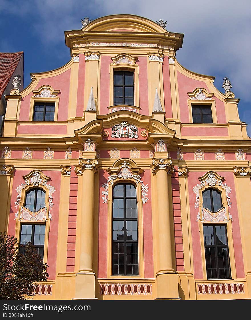 The picture shows an old, historic, baroque house facade in the city of Neuburg (Germany, Bavaria). The building is yellow and pink. There are ornaments around the windows. The image has a blue sky as background. The picture shows an old, historic, baroque house facade in the city of Neuburg (Germany, Bavaria). The building is yellow and pink. There are ornaments around the windows. The image has a blue sky as background.