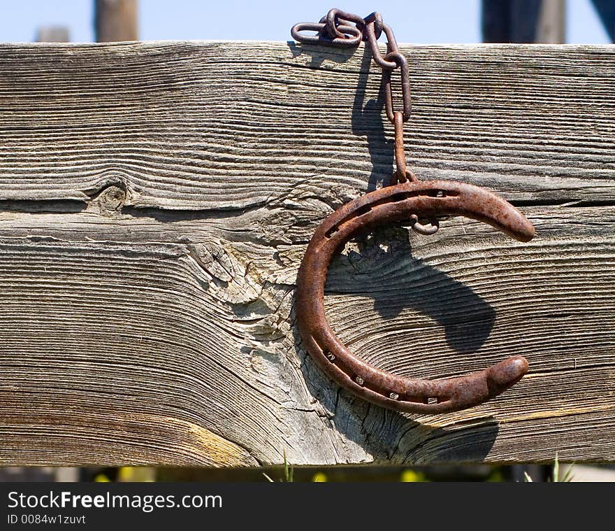 Rusty old horseshoe hanging by a rusty chain from a wooden fence. Rusty old horseshoe hanging by a rusty chain from a wooden fence