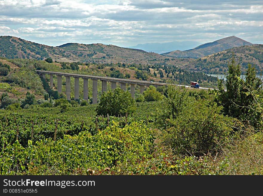 Macedonian landscape - road flyover towering over vast expanses of vineyards; hills and a lake in the background